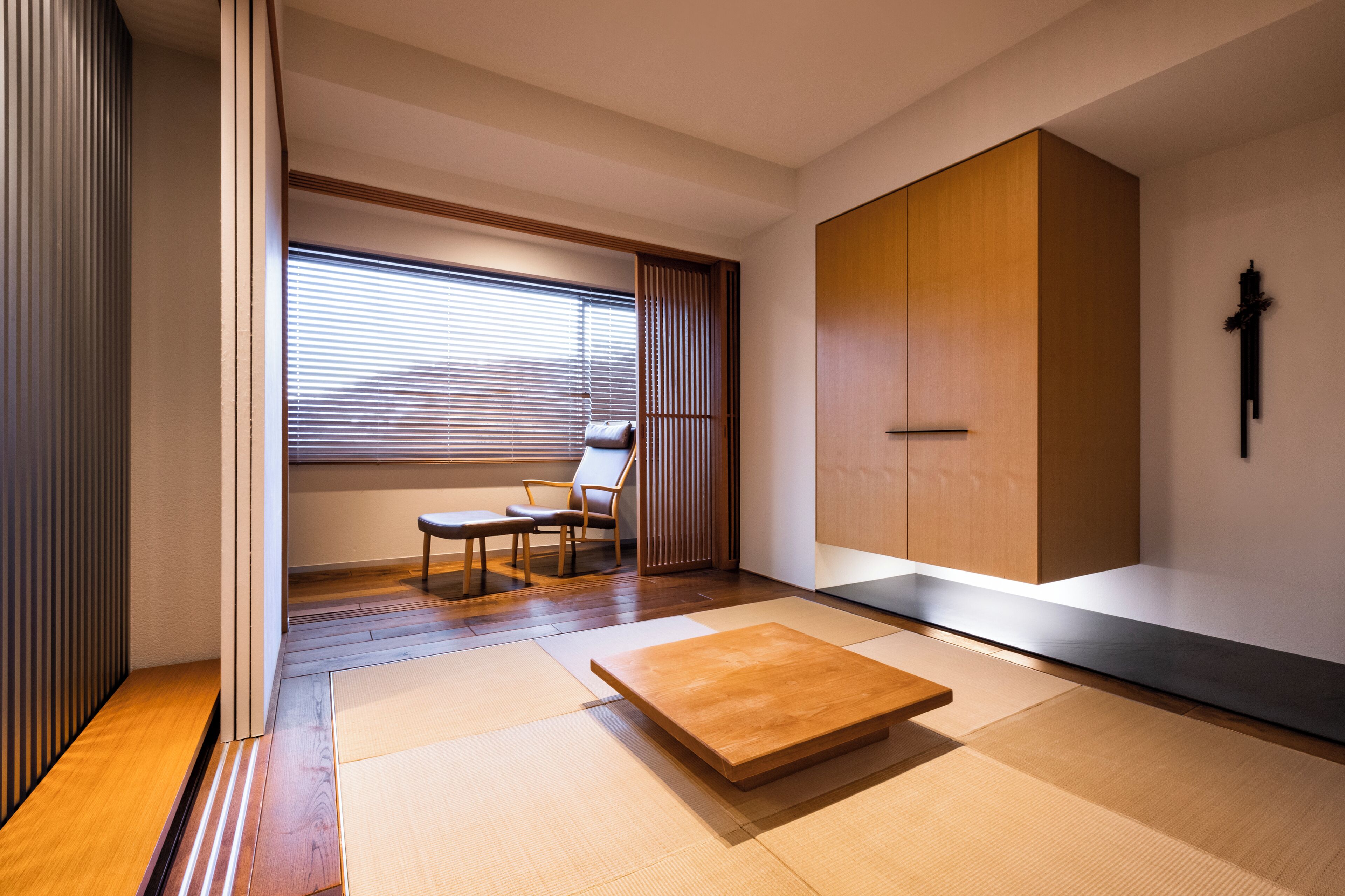 Um quarto japonês tradicional com tatames, uma mesa de madeira baixa, uma cadeira e portas corrediças.