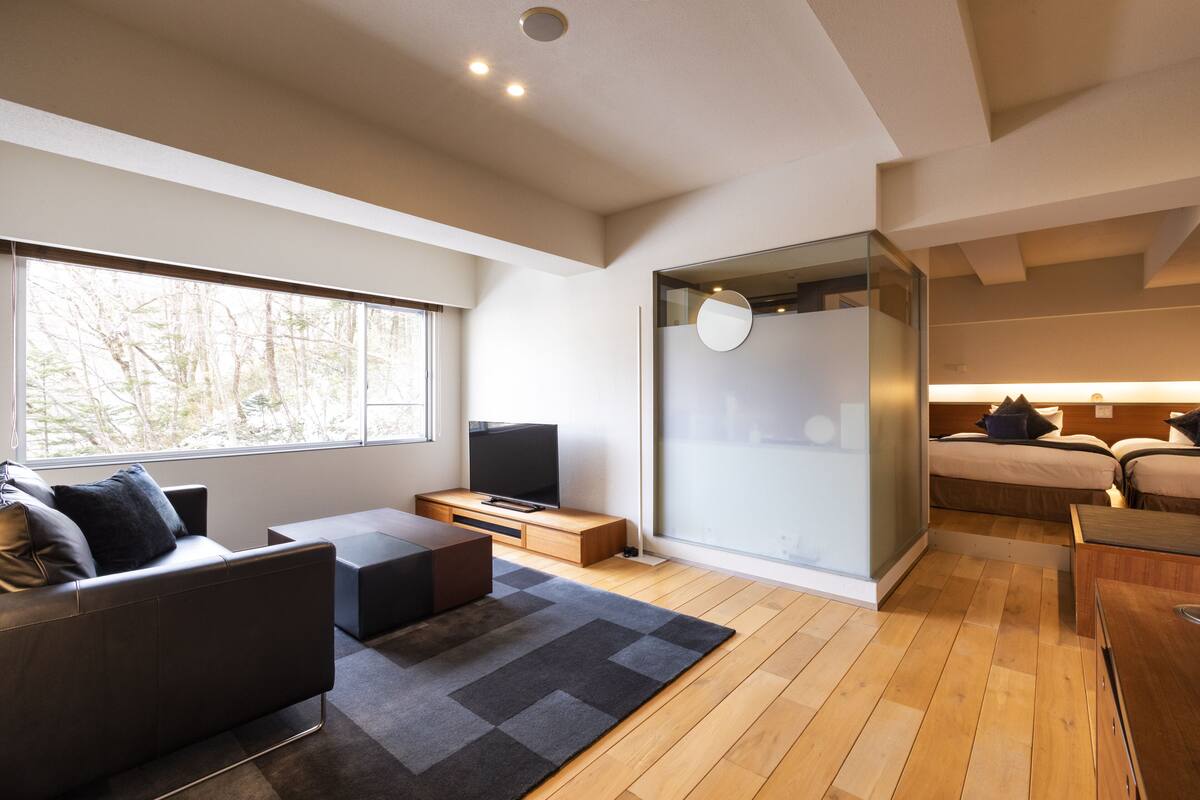 Un salon moderne avec un canapé, un téléviseur, un plancher en bois et une grande fenêtre.