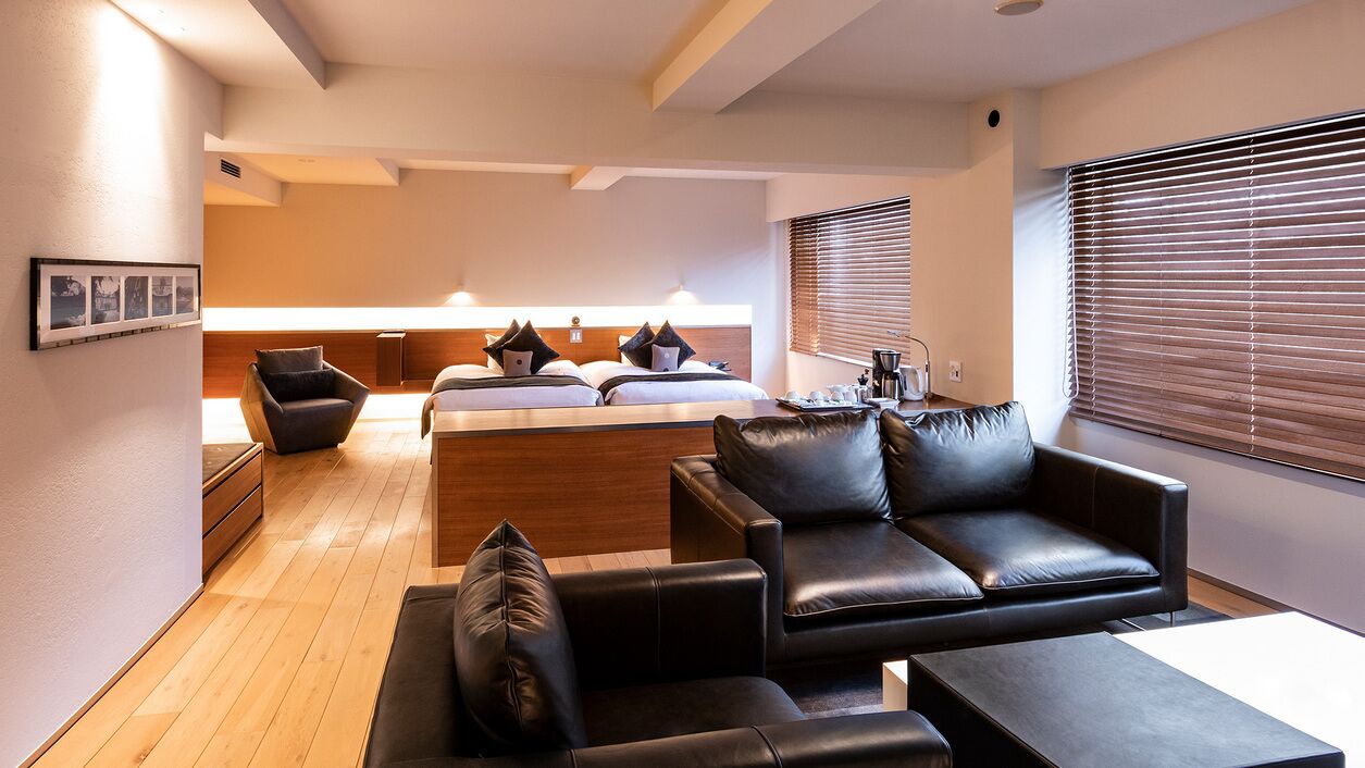 Una camera d'albergo moderna con pavimento in legno, un divano, un letto con cuscini, un tavolino e una finestra con persiane.