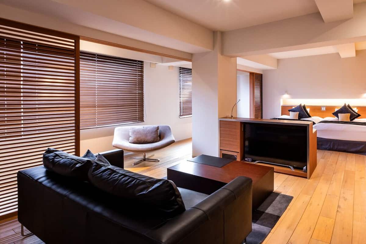 Une chambre d’hôtel moderne équipée d’un canapé, d’un fauteuil, d’une télévision, d’un lit et d’un bureau.