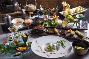 A variety of dishes and drinks on a table, including sushi, sashimi, and a teapot.