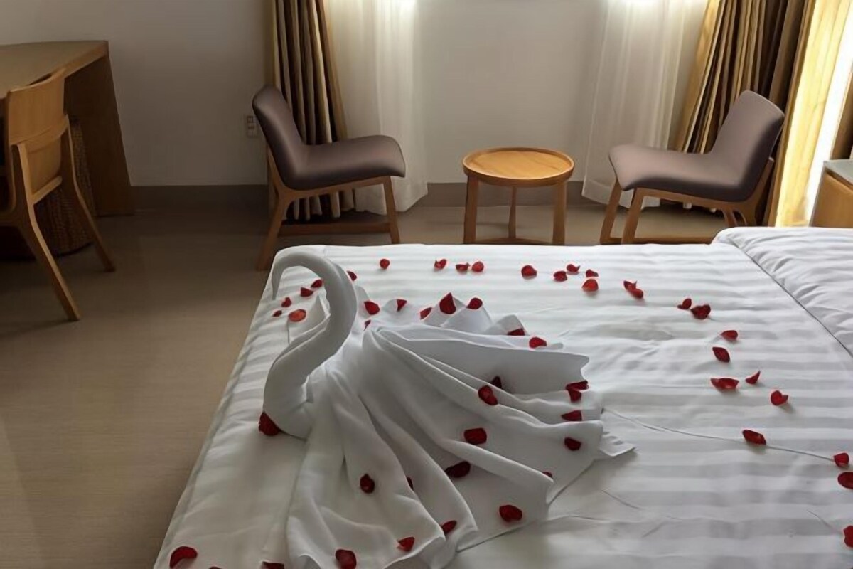 A hotel room with a bed, two chairs, a small round table, and curtains.