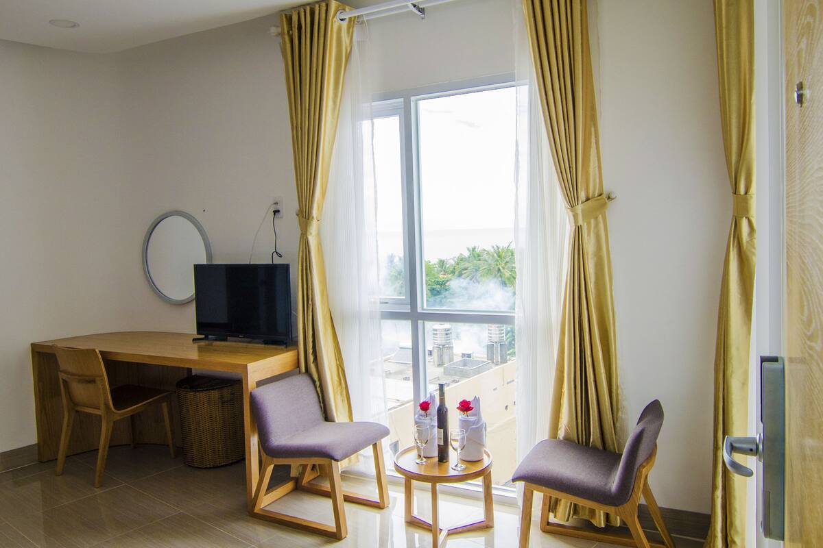 A hotel room with a wooden desk, two chairs, a television, and a window with curtains.