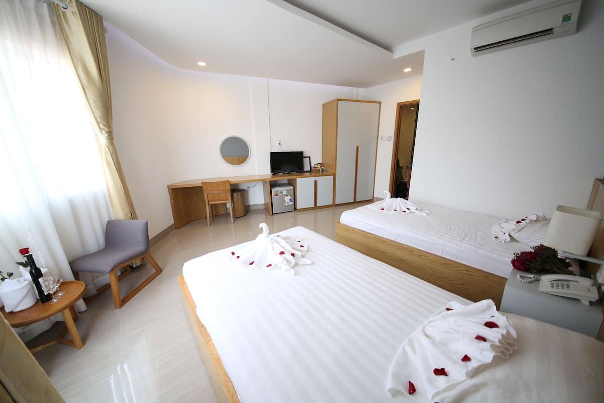 A hotel room with two beds, a desk, a chair, a small table, a mirror, and a phone.