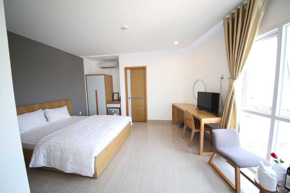 A hotel room with a bed, a desk, a chair, a television, and a window with curtains.