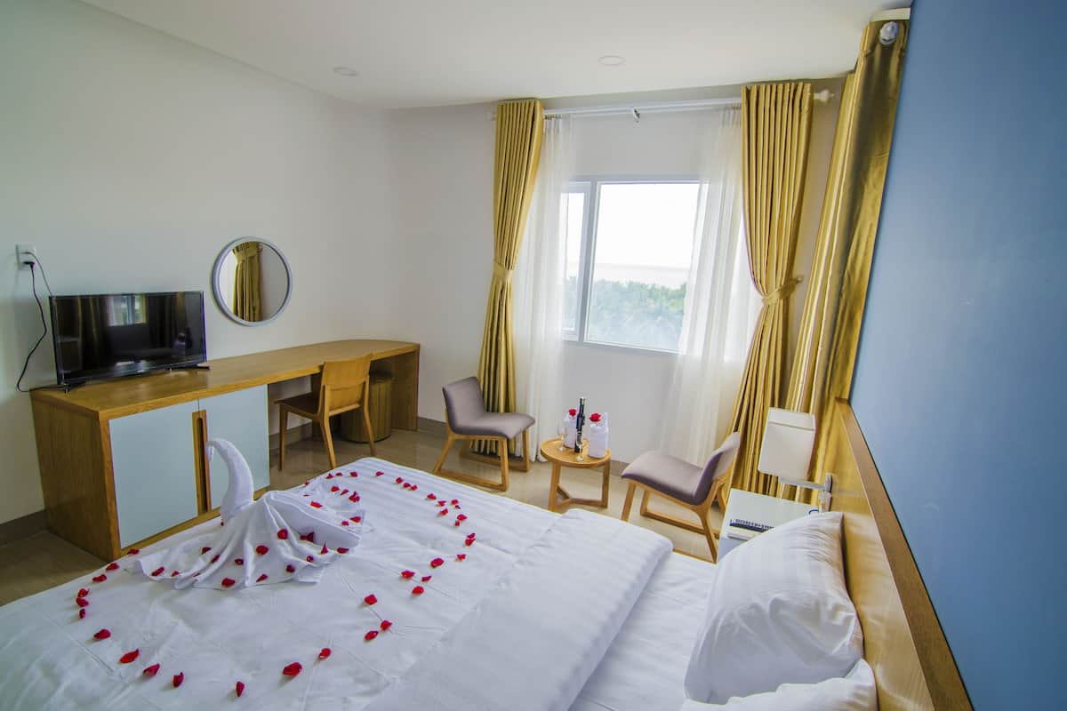 A hotel room with a bed, a desk, a chair, a TV, and a window with curtains.