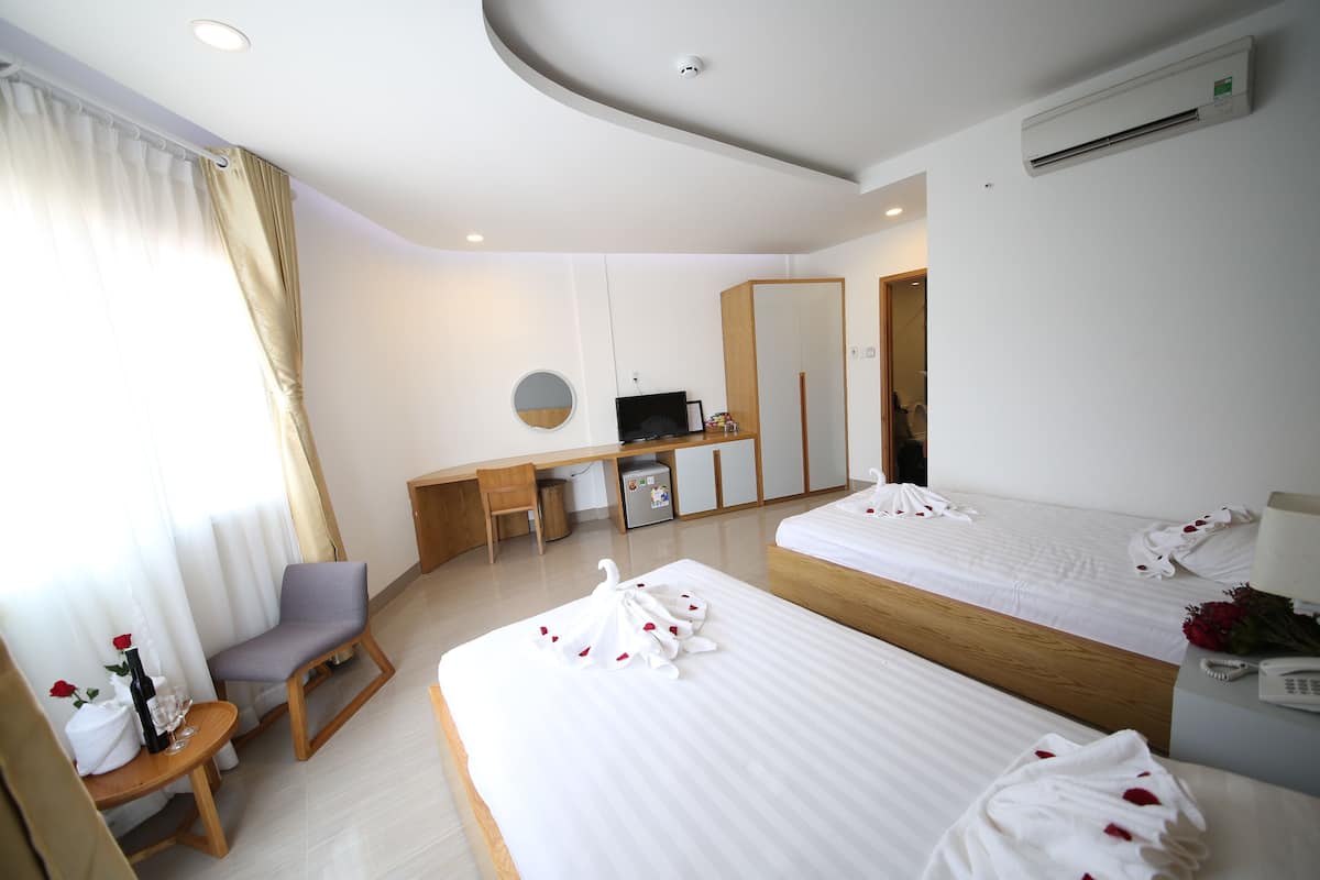 A hotel room with two beds, a desk, a chair, a small table with a bottle and glasses, and a TV.
