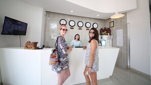 A reception area with a white counter, a television mounted on the wall, and several clocks above the counter. - Sailing Hotel (Phu Quoc)