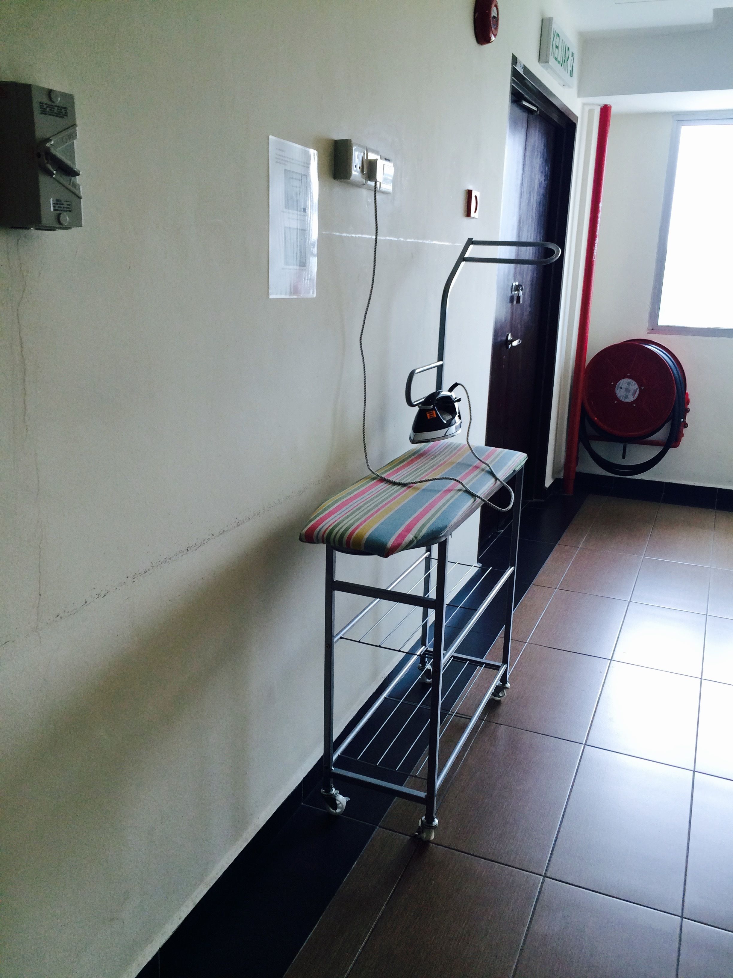 A corridor with a metal cart holding a striped cushion, a wall socket, a door, and a window.