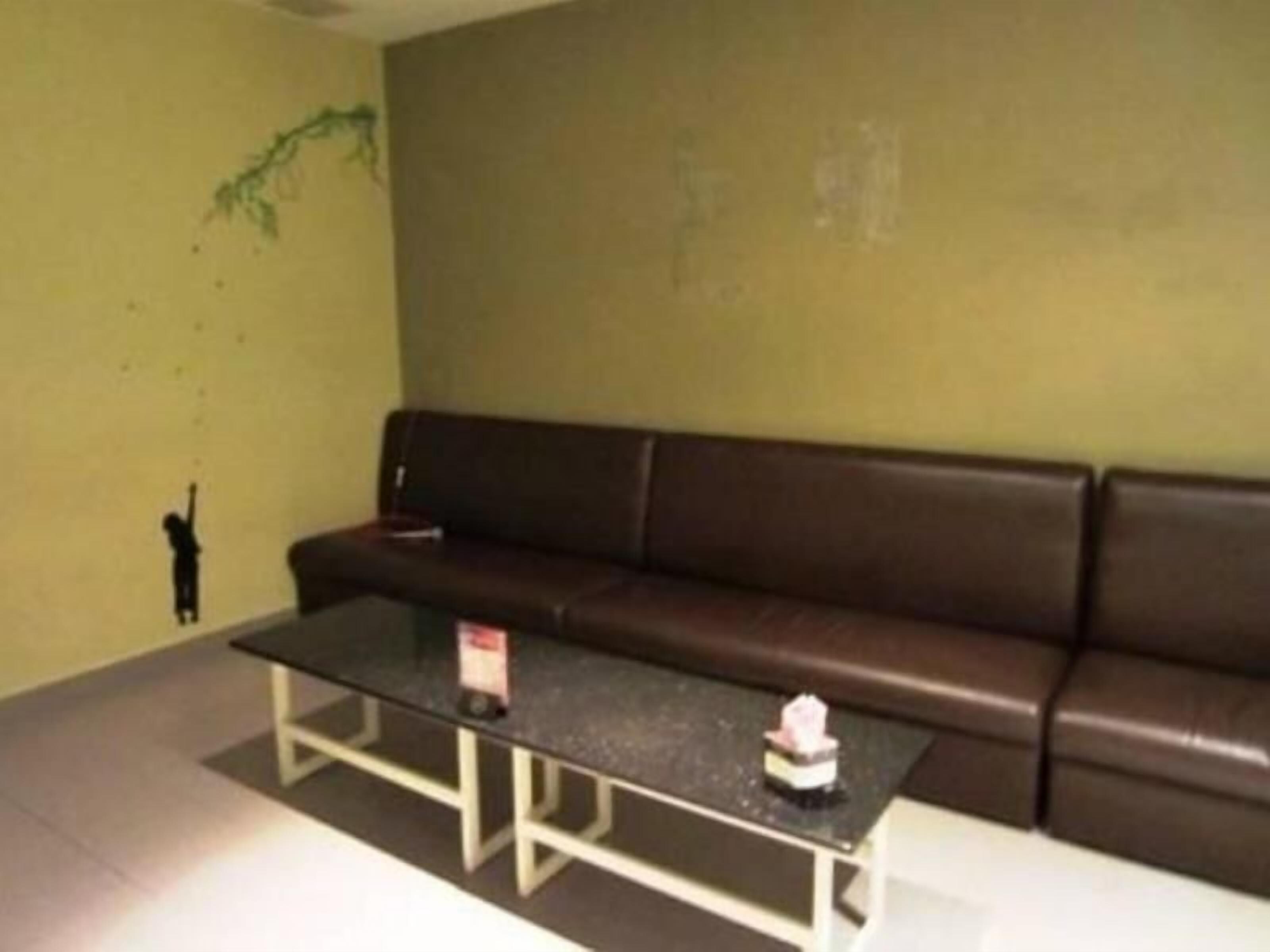 A room with a brown leather sofa, a glass coffee table, and a small table with a bottle.