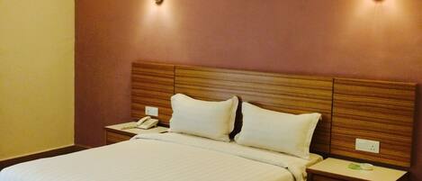 A hotel room with a large bed, wooden headboard, two bedside tables with lamps, a telephone, and a painting on the wall.
