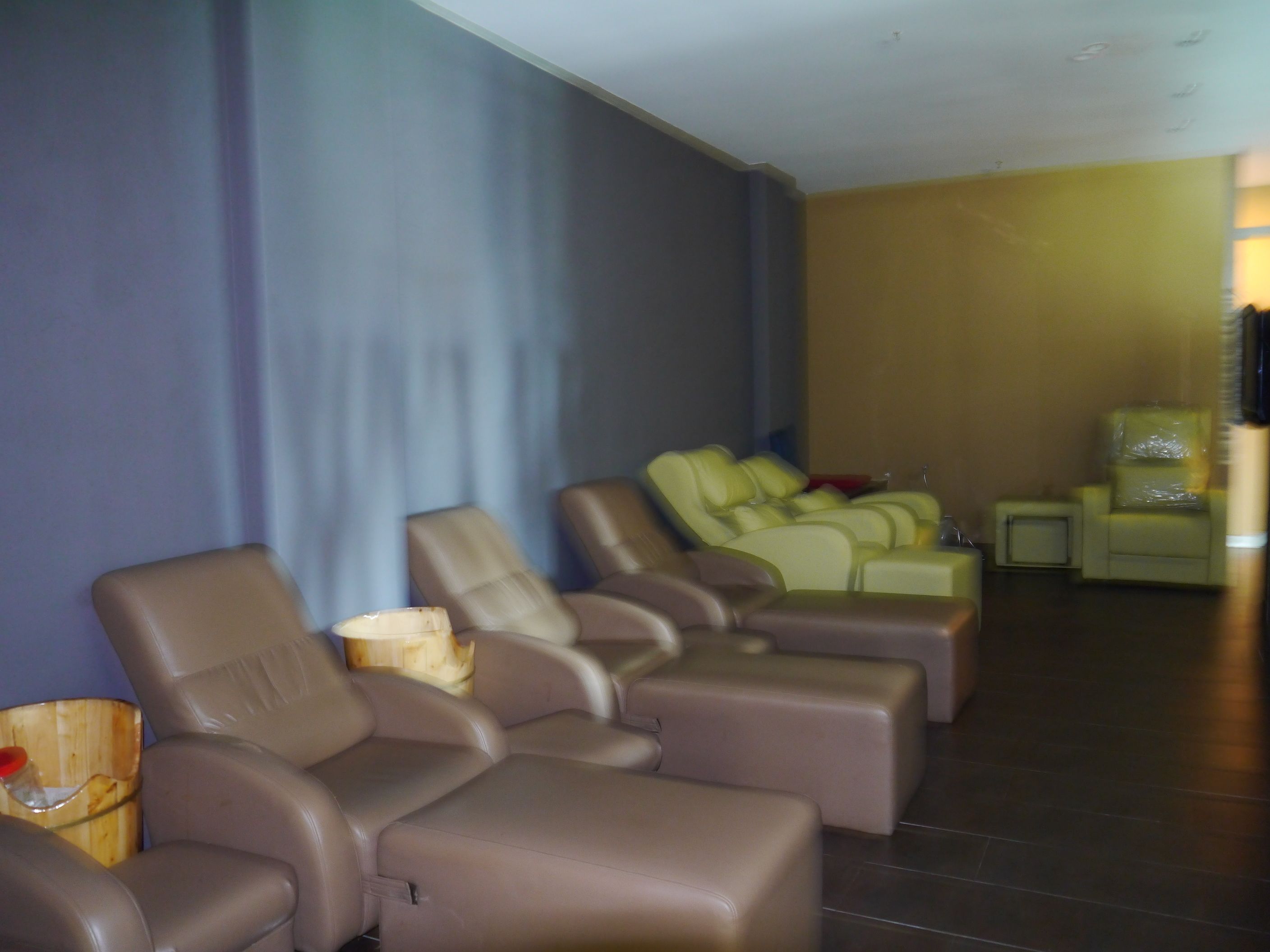 A room with multiple reclining chairs, a small table with a bottle, and a television on a stand.