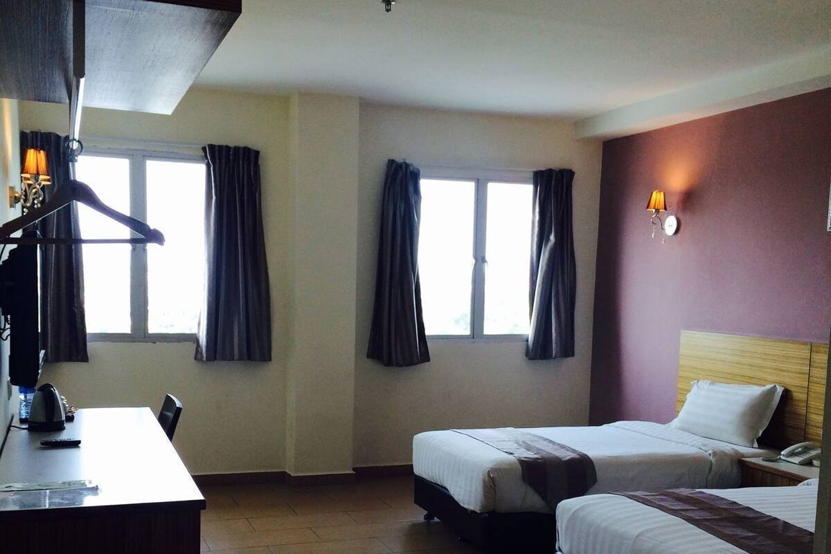 A hotel room with two beds, a desk, a lamp, and a window with curtains.