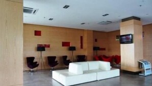 A modern lobby with a white sofa, red chairs, and a TV mounted on the wall.