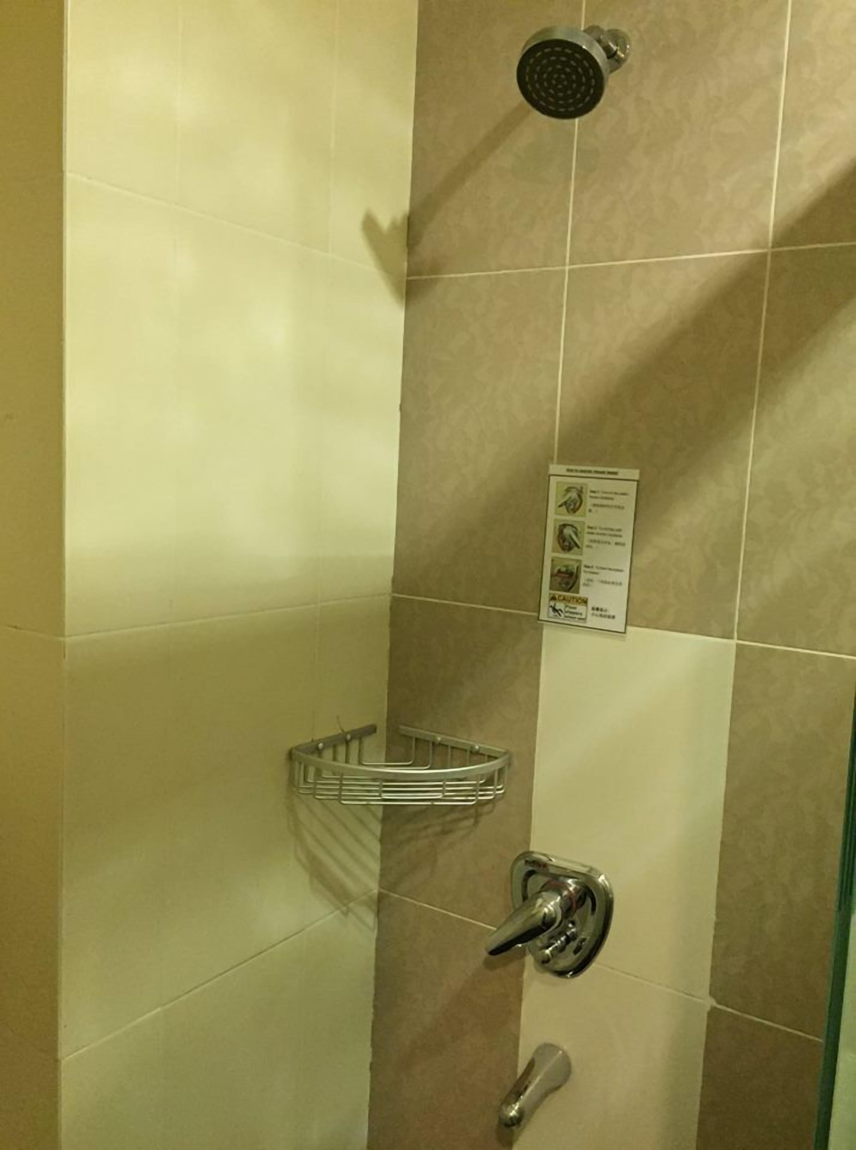 A shower area with a handheld showerhead, a wall-mounted control panel, and a metal shelf.