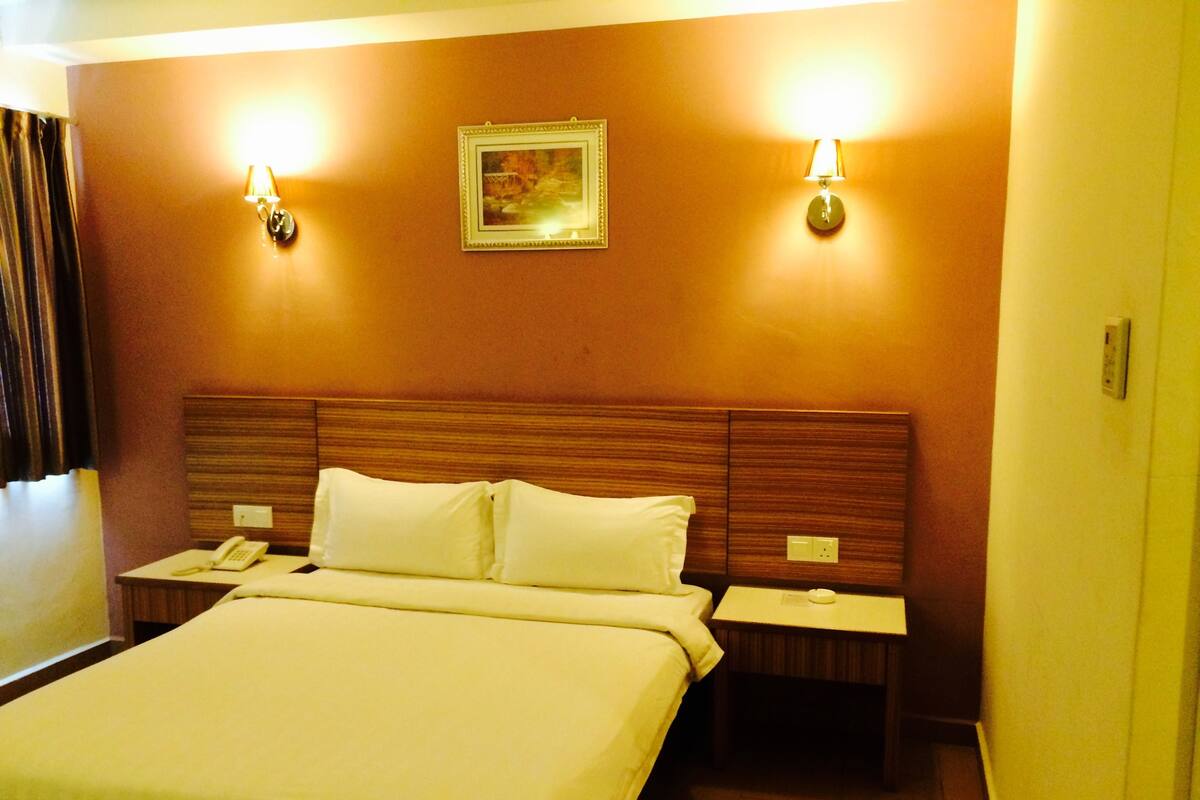 A hotel room with a large bed, two bedside tables, a telephone, and two wall-mounted lamps.