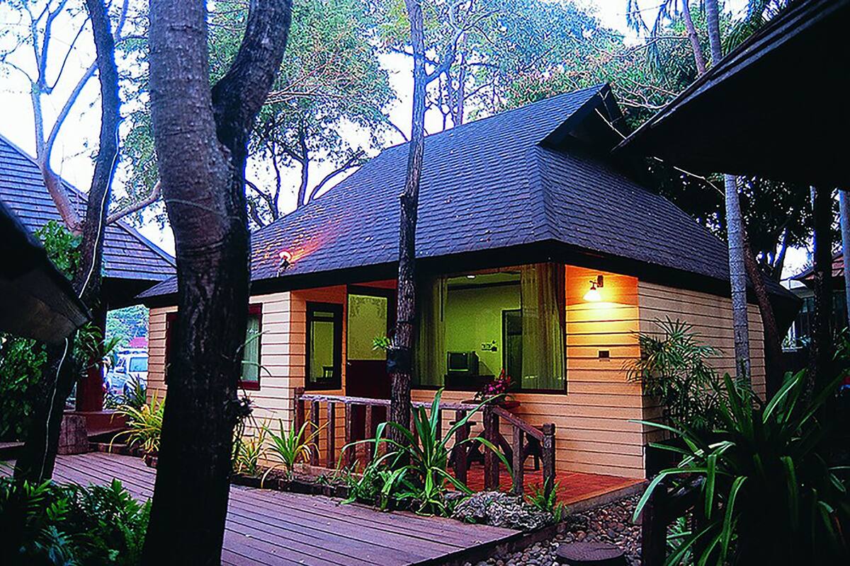 Een houten huis met een veranda, omringd door bomen en planten.