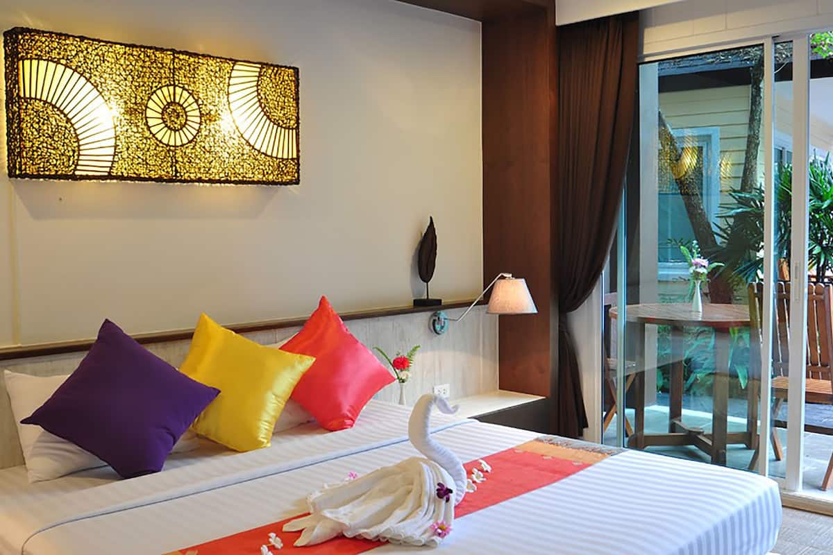 Hotelkamer met een bed, kleurrijke kussens, decoratie in de vorm van een zwaan, een wandlamp en uitzicht op het groen door een glazen deur.