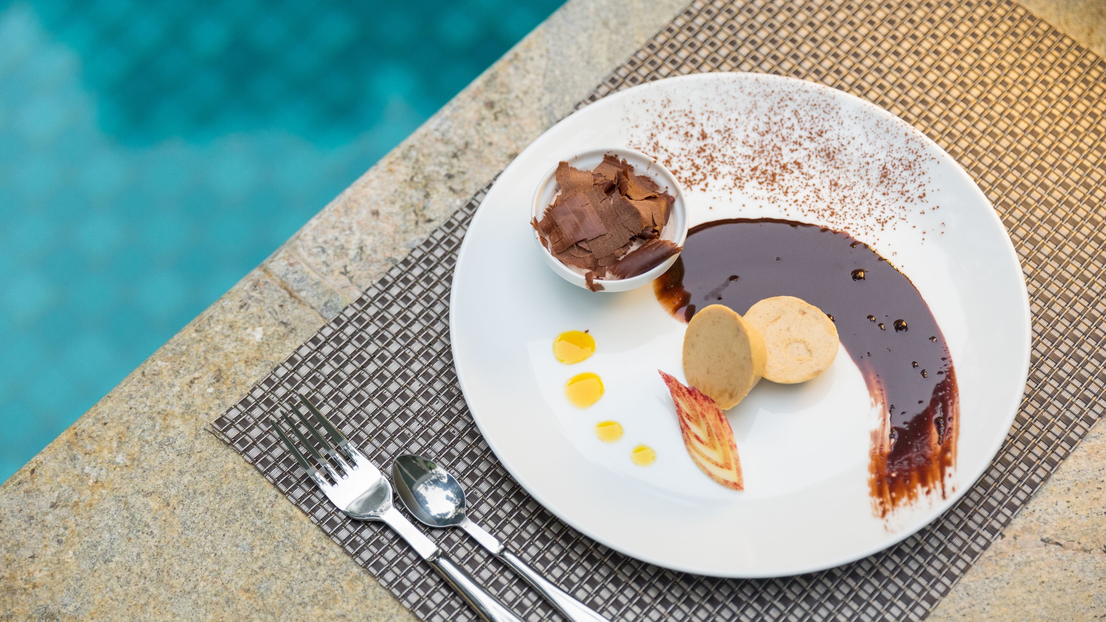 Un plato de postre con chocolate y salsa, colocado sobre una mesa cerca de una piscina.