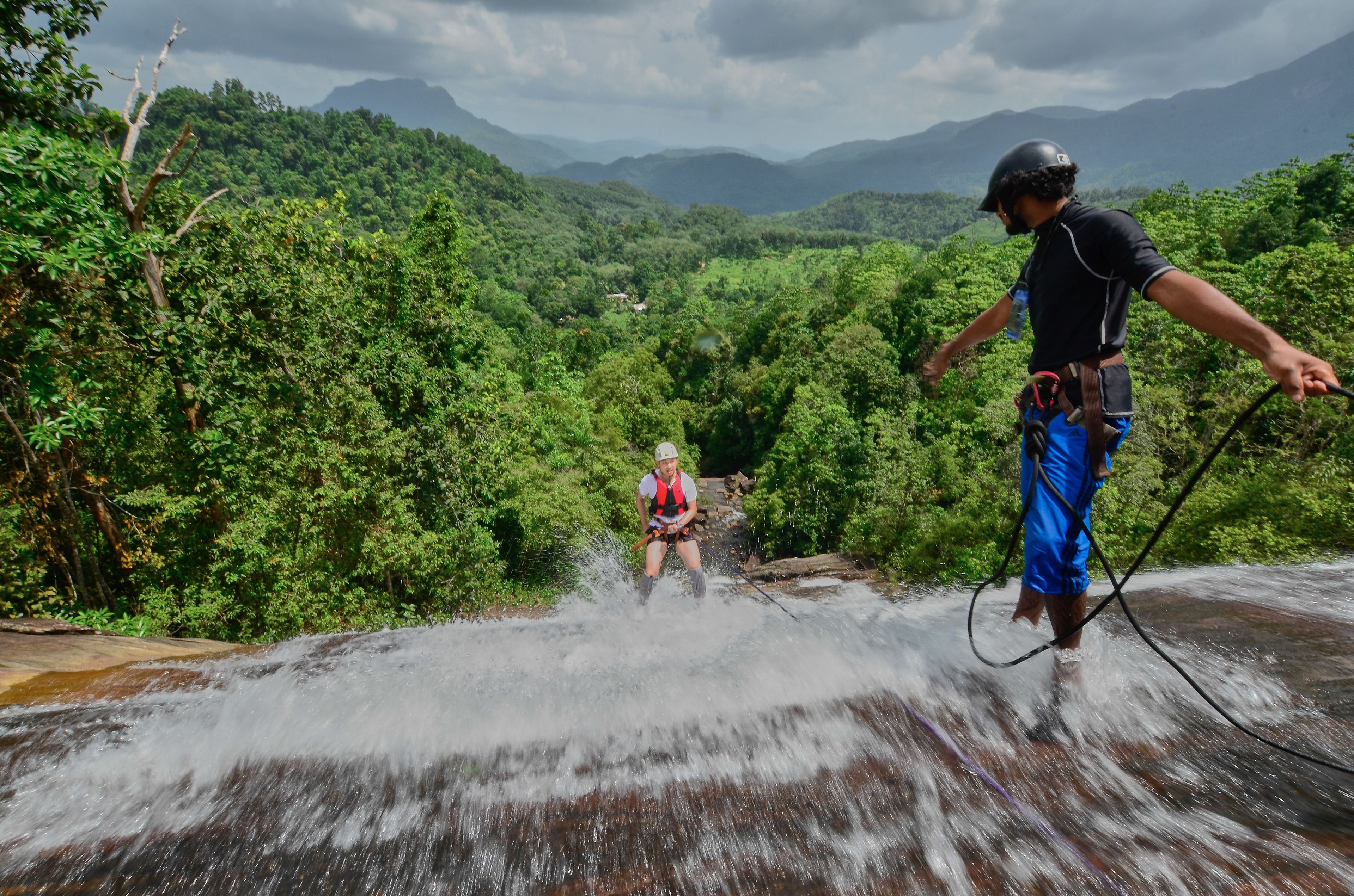 A person rappelling down a waterfall in a lush, green forested area.
