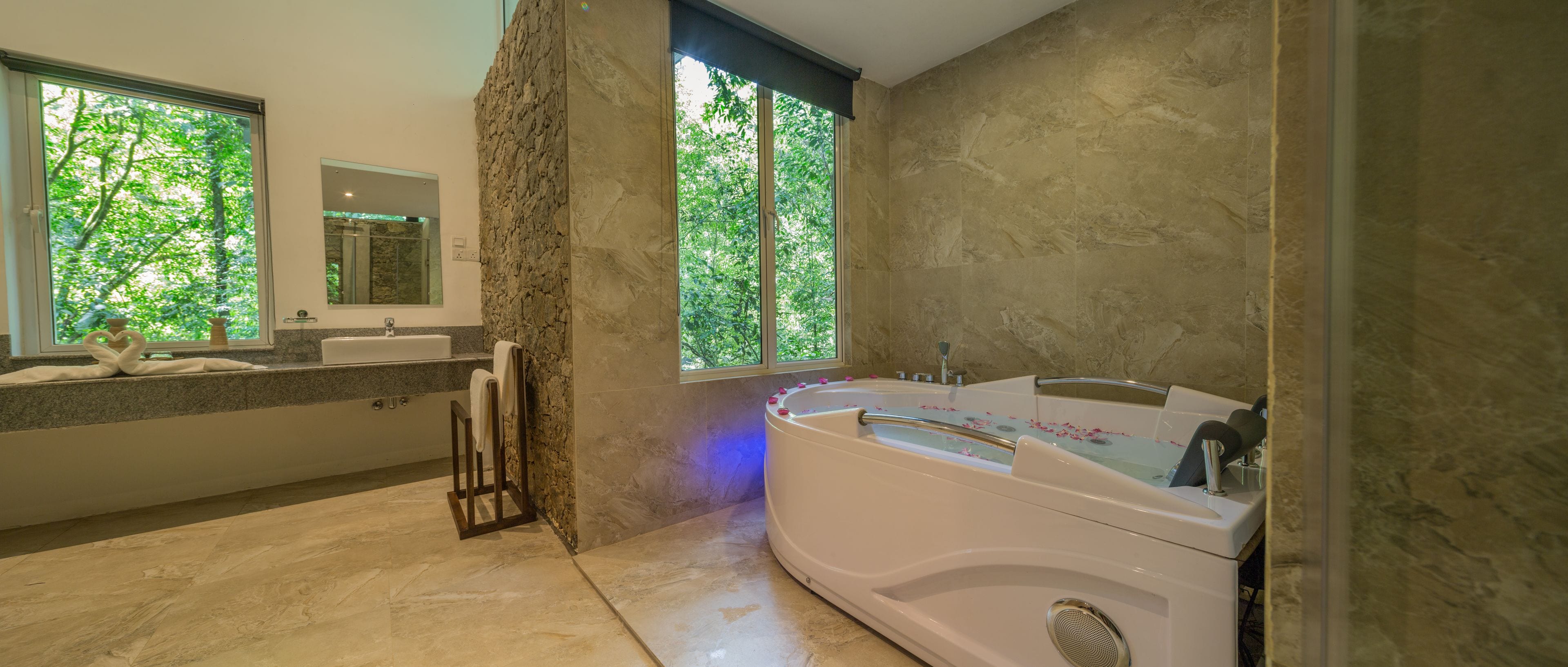 Un baño moderno con una bañera grande, un tocador con espejo y una ventana con vistas a árboles.