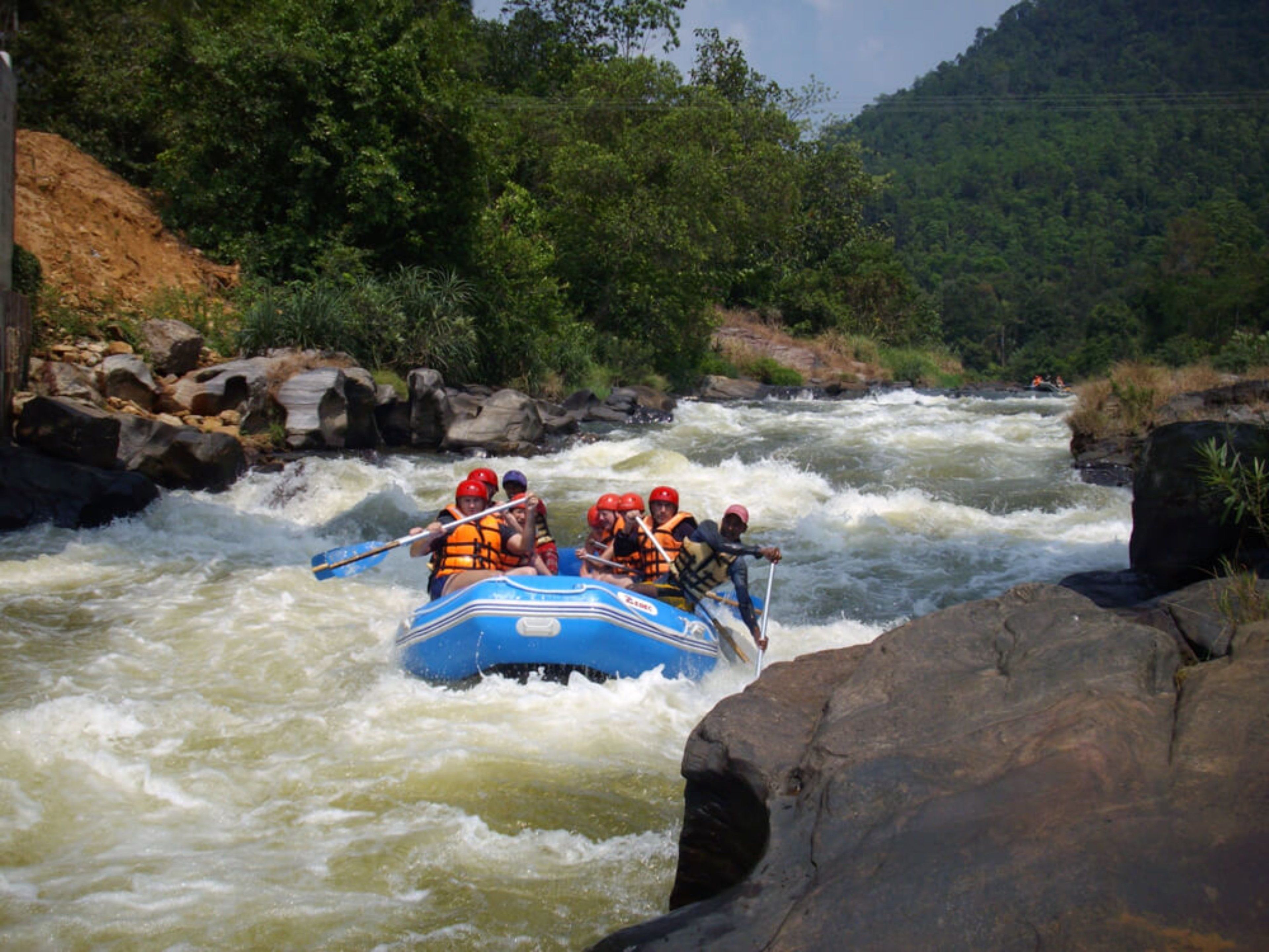 A group of people in a blue raft navigating a river with rapids.