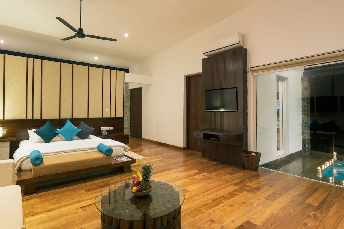 A modern bedroom with a bed, a glass coffee table, a ceiling fan, and a view of a swimming pool.