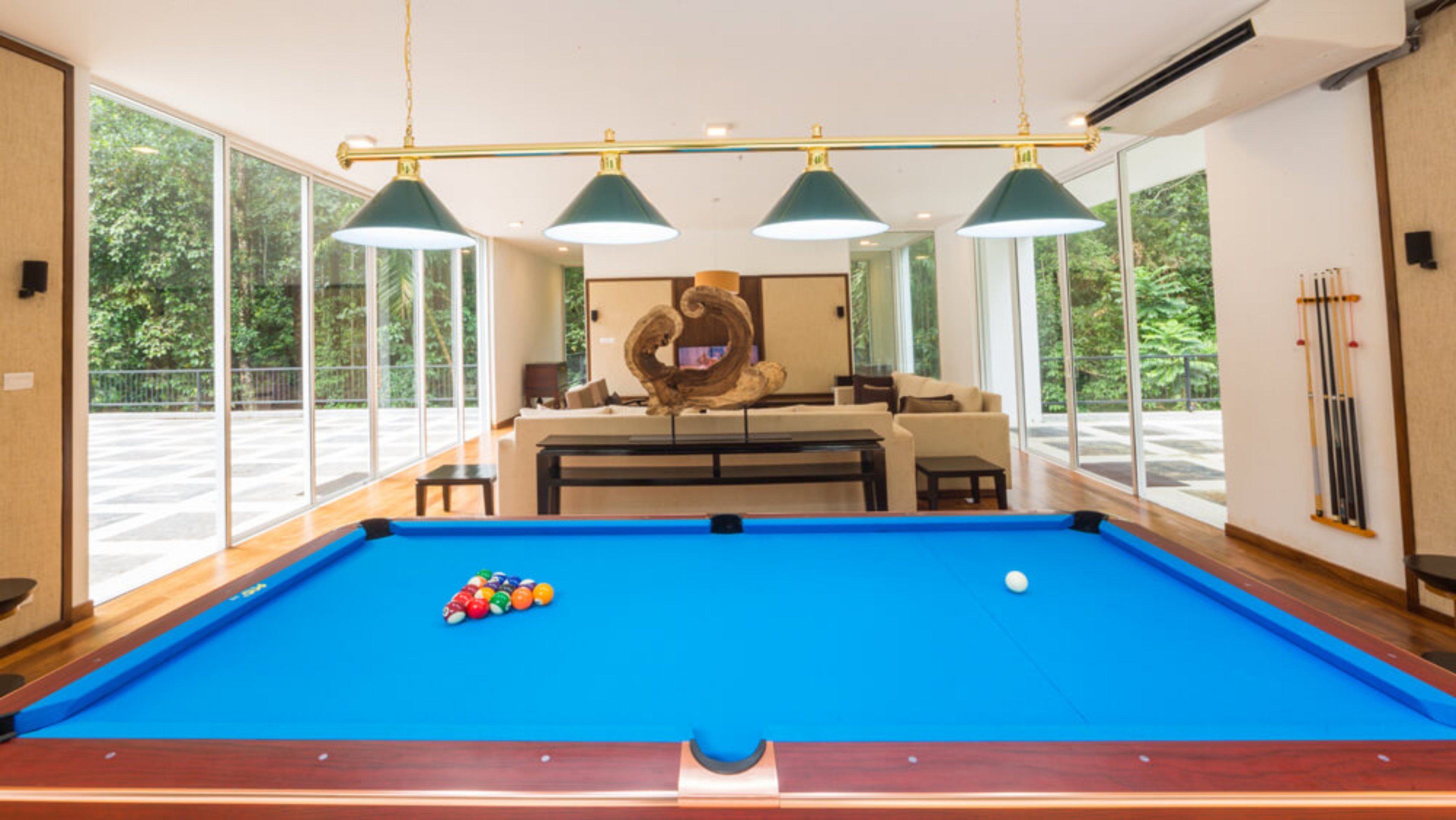 A pool table with balls, a sofa, a coffee table, and a decorative sculpture in a room with large windows and hanging lamps.