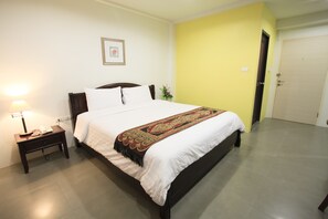 A neatly made bed with a white and red bedspread, a bedside lamp, and a nightstand with a phone. - Su 22 (Bangkok)