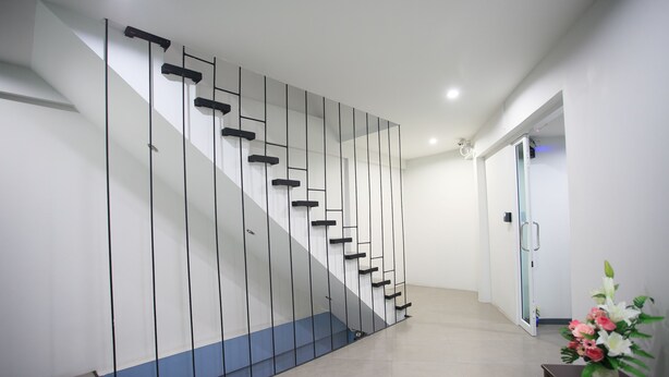 A modern staircase with a minimalist design, a door leading to another room, and a small table with a vase of flowers. - Su 22 (Bangkok)