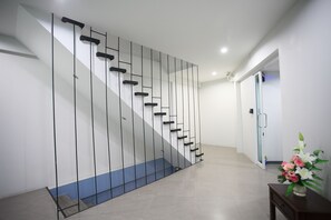 A modern staircase with a minimalist design, a door leading to another room, and a small table with a vase of flowers. - Su 22 (Bangkok)