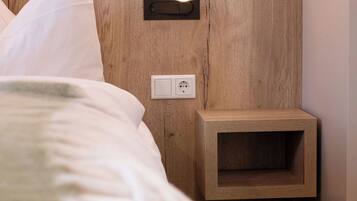 Una cama bien hecha con ropa de cama blanca, una mesita de noche con toma de corriente e iluminación de pared.
