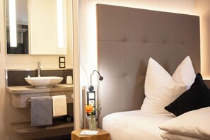 A hotel room with a large bed, a headboard, a bedside table with a lamp, a mirror, a sink, and a towel. - weila - dein Boutiquehotel (Arnsberg)