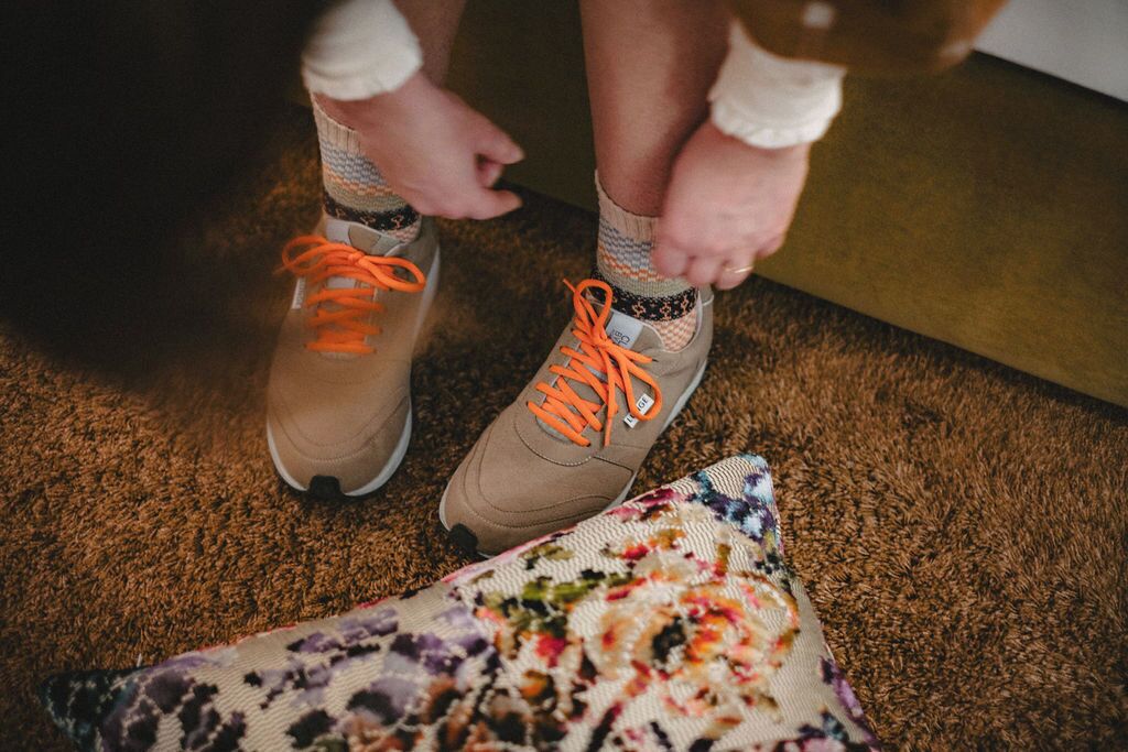 A pair of brown shoes with orange laces being tied.