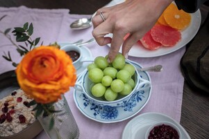 Una mesa con un bol de uvas verdes, un plato con mandarinas en rodajas y un bol de compota de frutos rojos.