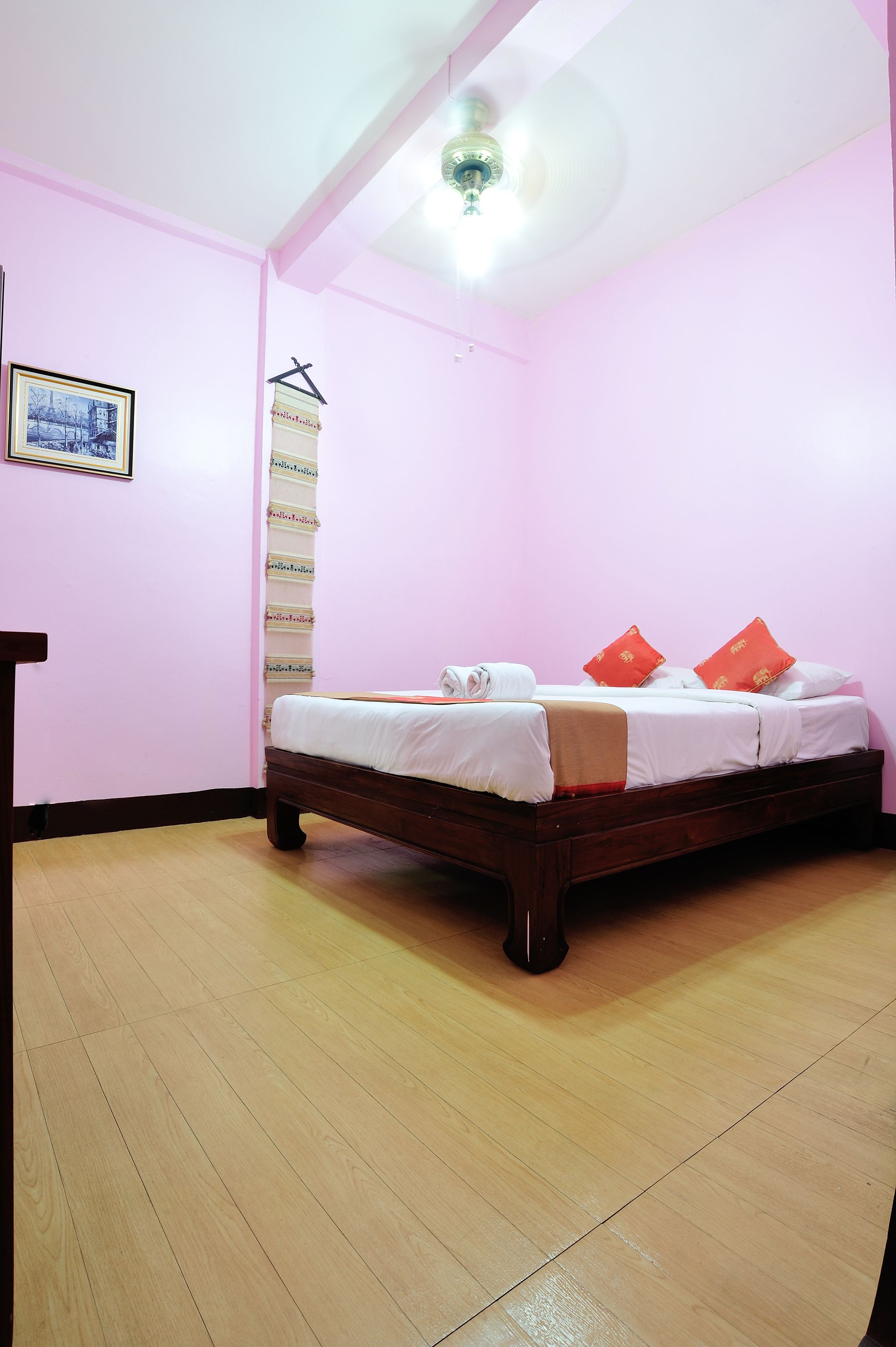A bedroom with a wooden bed, pink walls, and a ceiling fan.