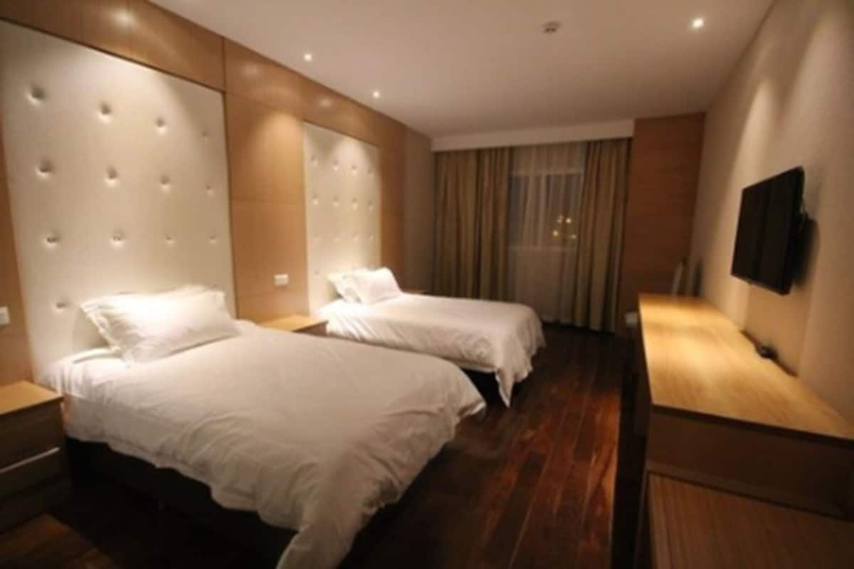 Habitación de hotel con dos camas, suelo de madera, un espejo grande y un televisor en la pared.