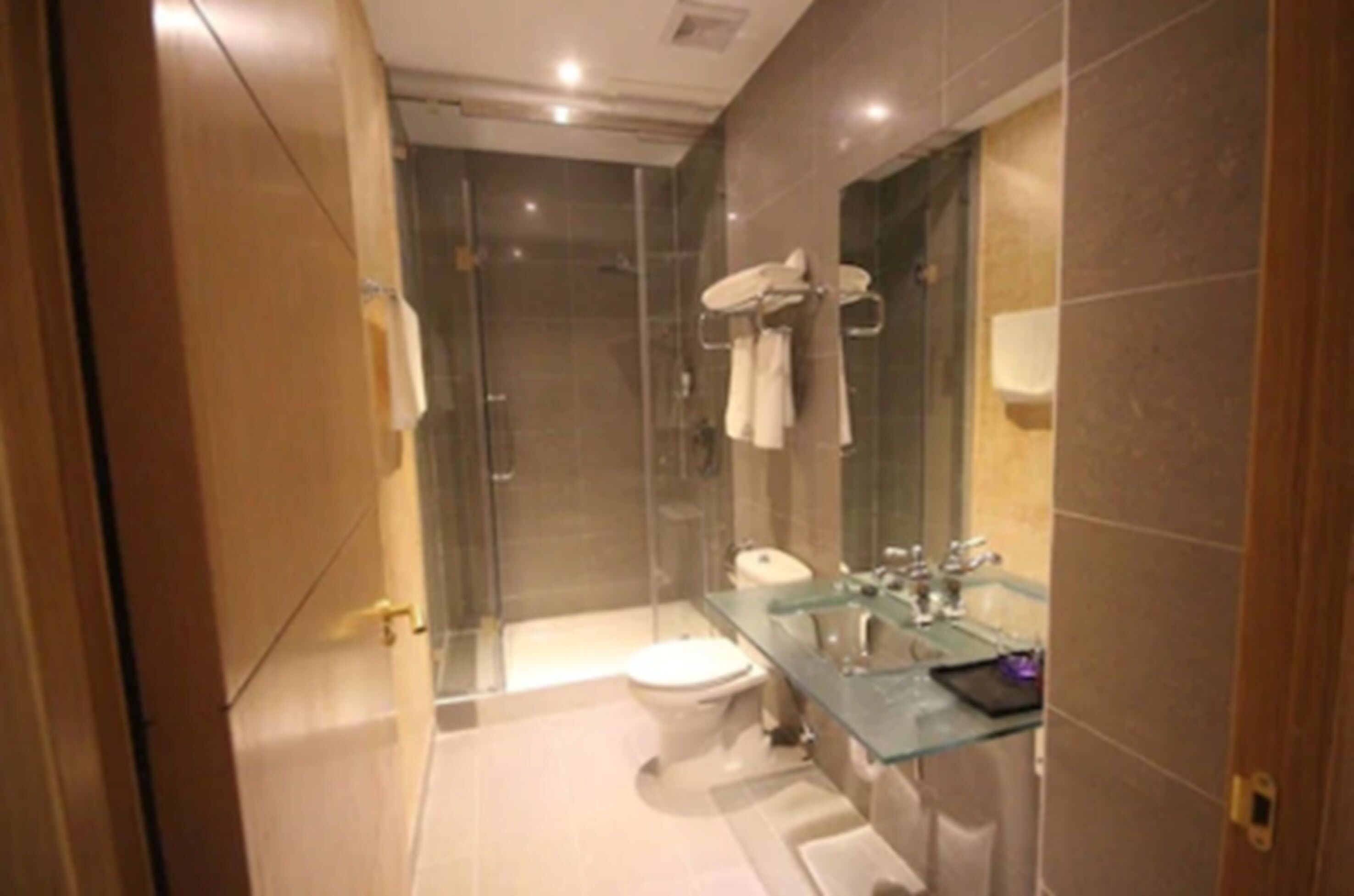 Un baño moderno con cabina de ducha de vidrio, lavamanos de vidrio y un inodoro.