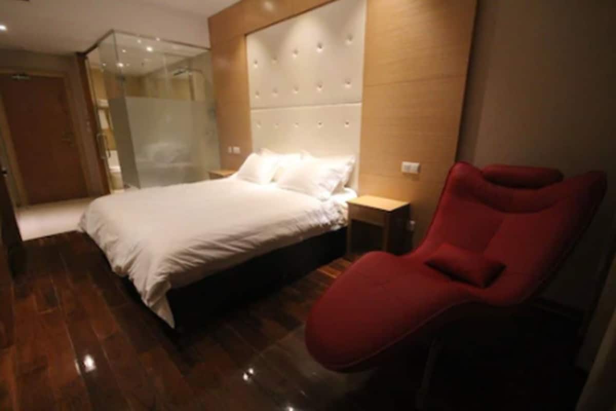Una habitación de hotel moderna con una cama grande, cabina de ducha de vidrio y una silla roja.