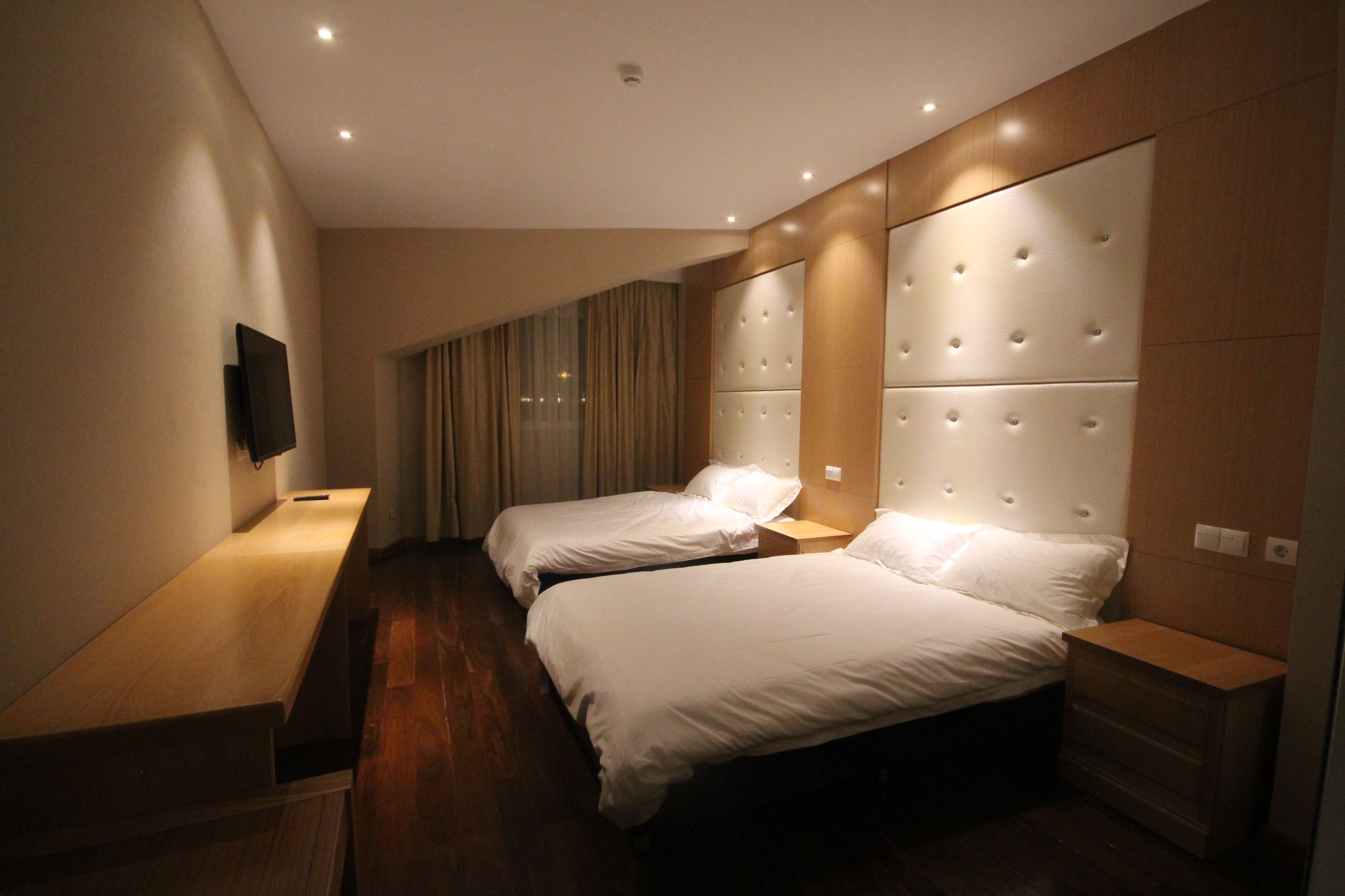 Een moderne hotelkamer met twee bedden, een flatscreen televisie aan de muur en een houten bankje.