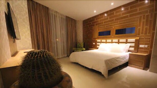 Een slaapkamer met een groot bed, een houten hoofdeinde, een nachtkastje en een cactus op een tafel.
