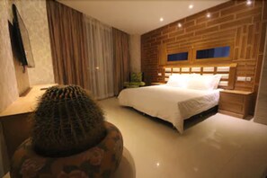 A bedroom with a large bed, a wooden headboard, a nightstand, and a cactus on a table. - Hotel Menoir Dorsett (Leganes)