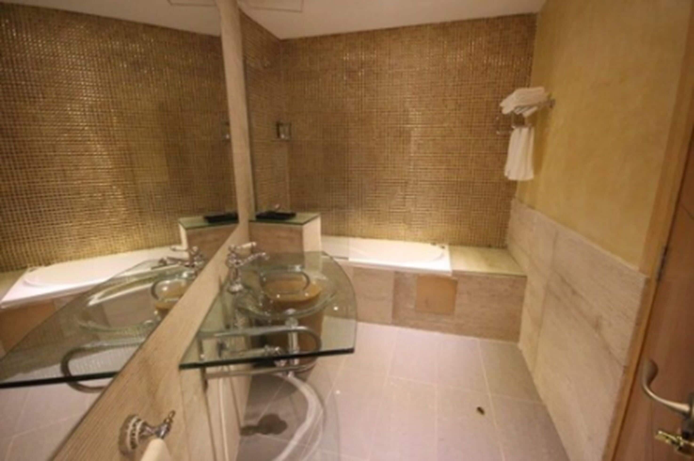 A bathroom with a glass vanity, a bathtub, and a mirror.