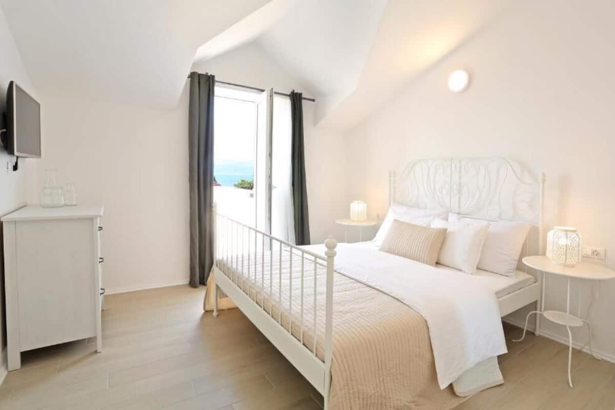 Un dormitorio con cama, mesita de noche y televisor montado en la pared.