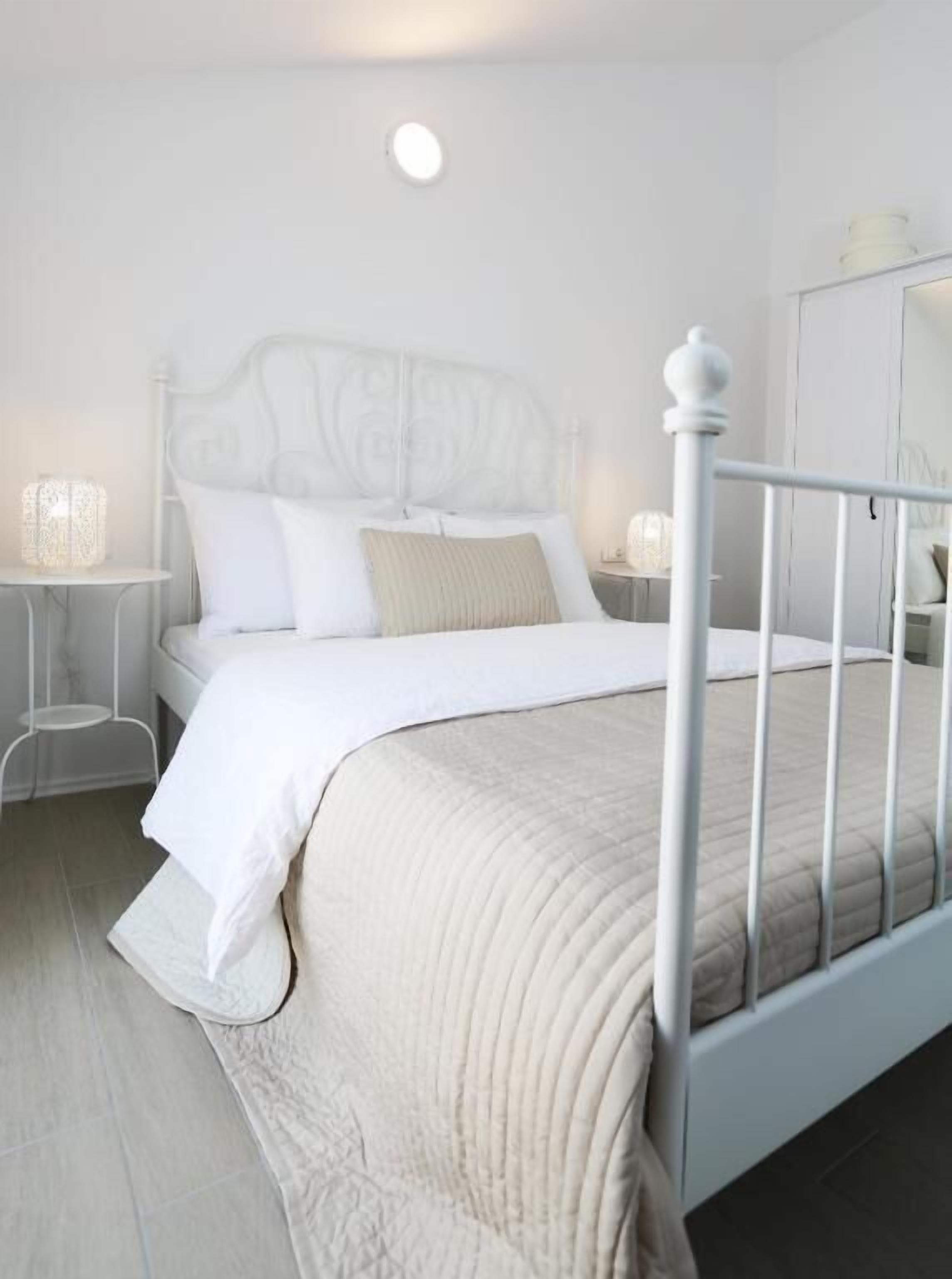 A neatly arranged bedroom with a white bed, a bedside table with a lamp, and a wardrobe.
