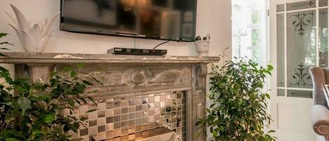 A living room with a fireplace, a flat-screen TV mounted above it, and a potted plant to the right.