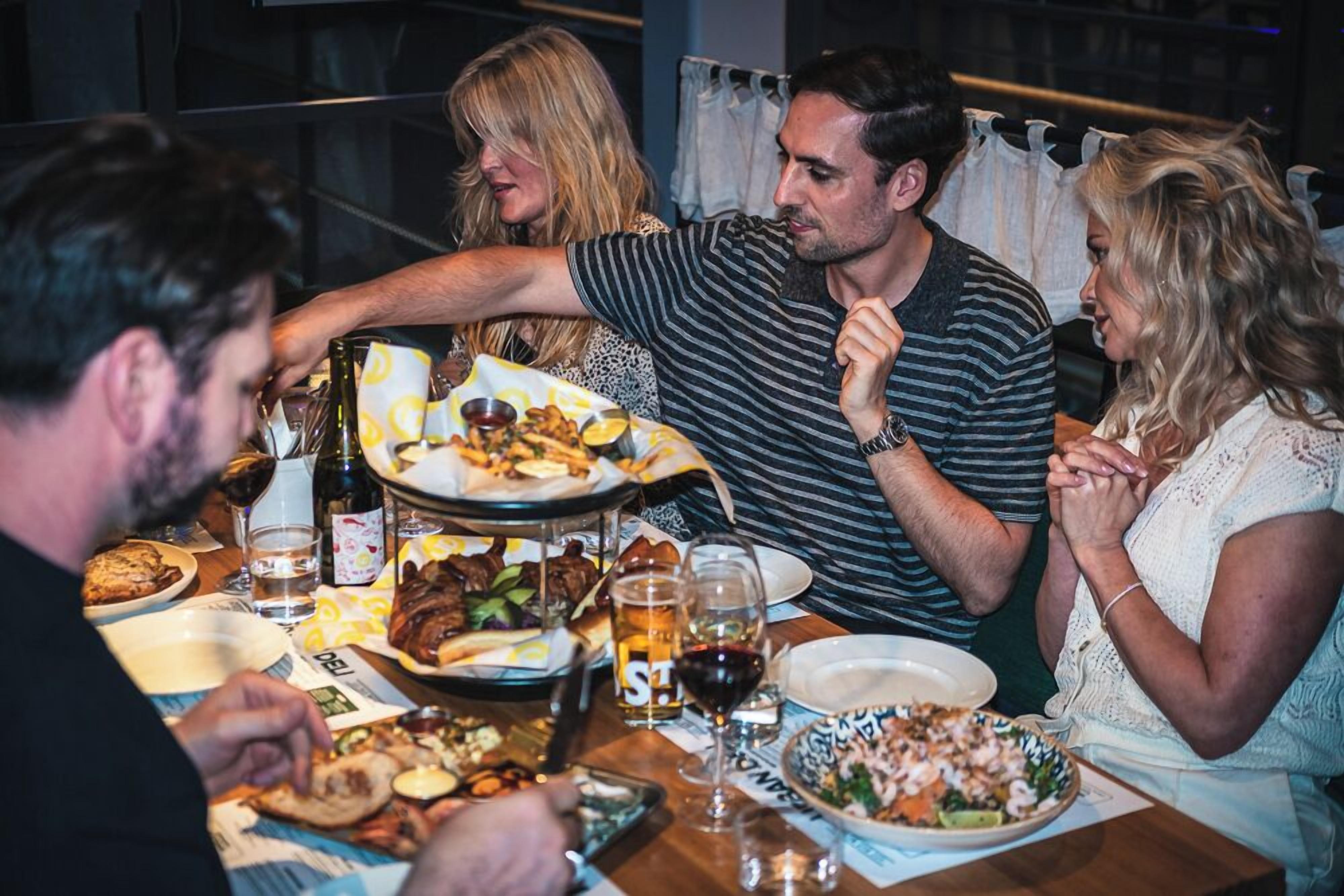 Een groep mensen dineert in een restaurant, met diverse gerechten en drankjes op tafel.