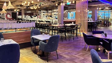 Interior de un restaurante con varias mesas, sillas y una zona de bar con estantes llenos de botellas.