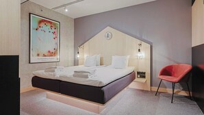 A modern bedroom with a bed, a red chair, and a wall-mounted artwork. - Hotel With Urban Deli (Stockholm)