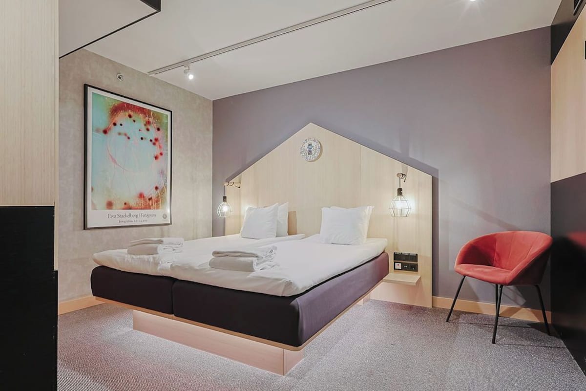 Un dormitorio moderno con una cama, una silla roja y una obra de arte colgada en la pared.